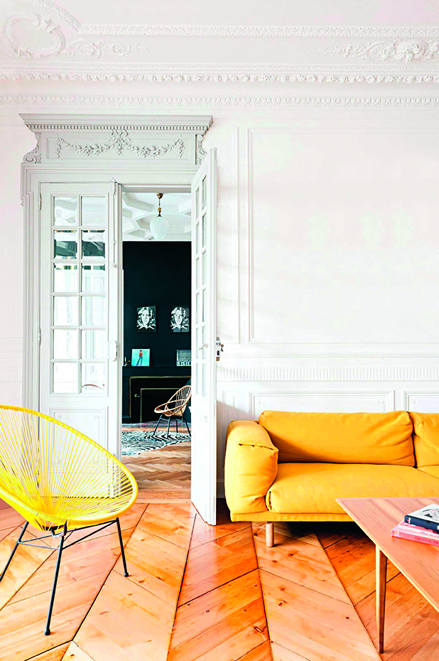 Salón con molduras y puerta con cristal tipo espejo y sofá amarillo. 
