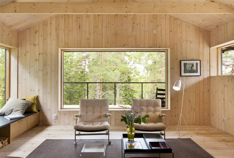 Interior recubierto de madera con alfombra y cojines en tonalidades cálidas.