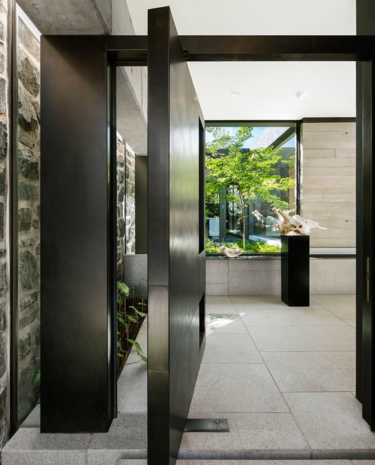 Gran estructura de puerta de acceso negra hacia interior de vivienda con pared de piedra, suelo de granito