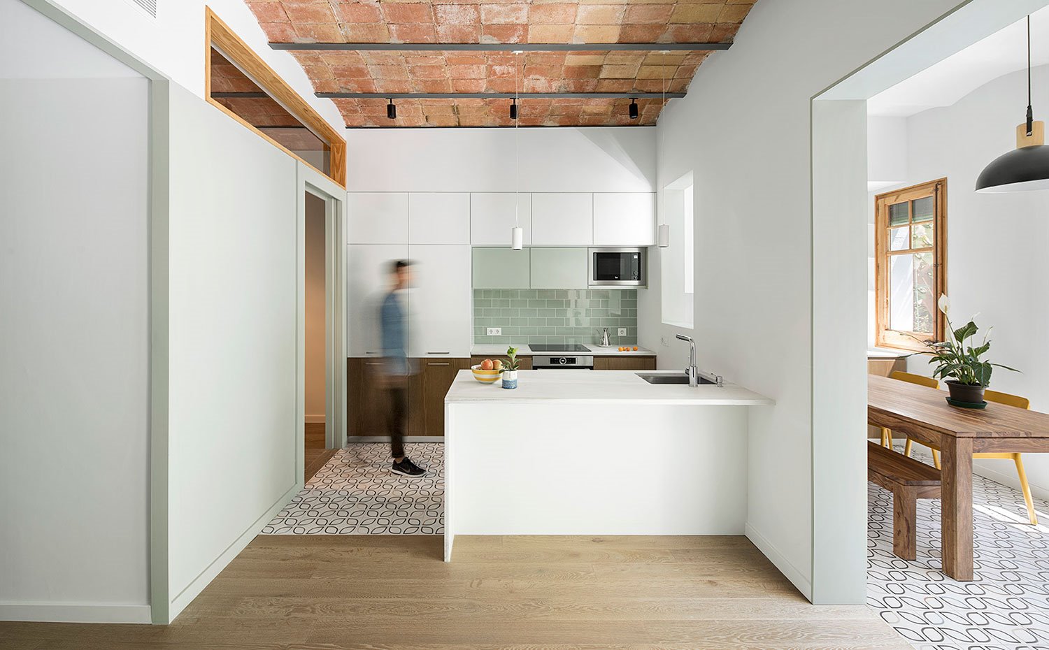 Cocina abierta con península, mobiliario en blanco, techo con bóveda catalana con apertura a comedor