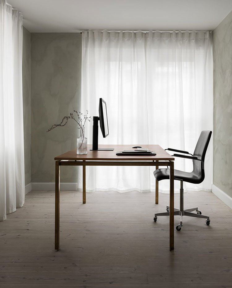 Zona de trabajo con mesa y silla en el centro de la estancia, suelo madera, cortinas blancas frente a ventanales