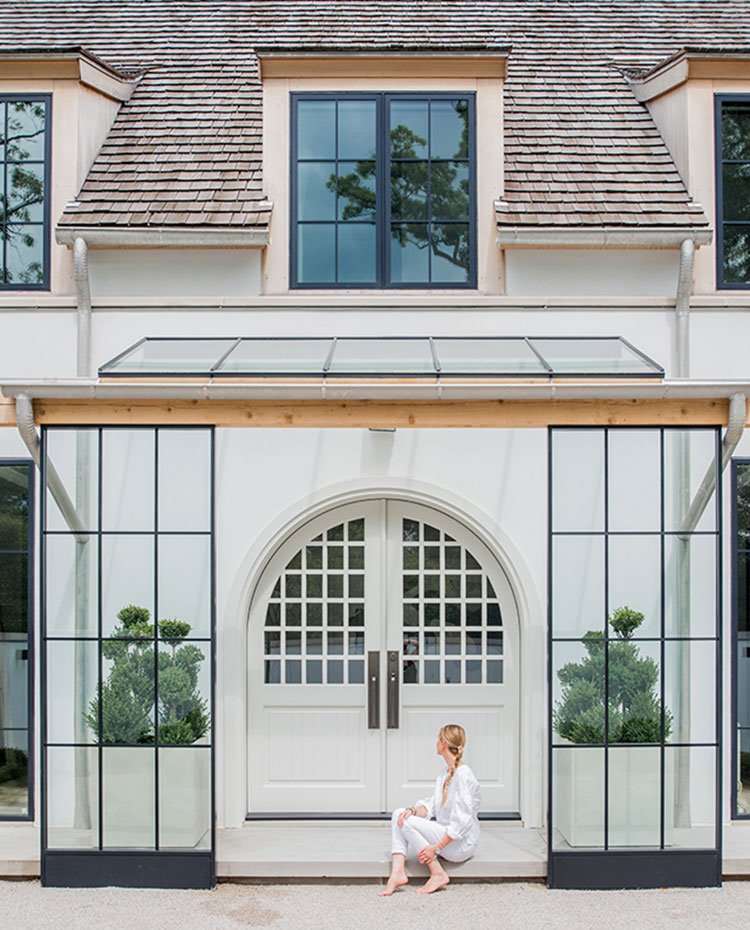 Acceso entrada en vivienda con puerta en blanco con arcada con cerramientos de cristal y grandes maceteros con plantas flanqueándola 
