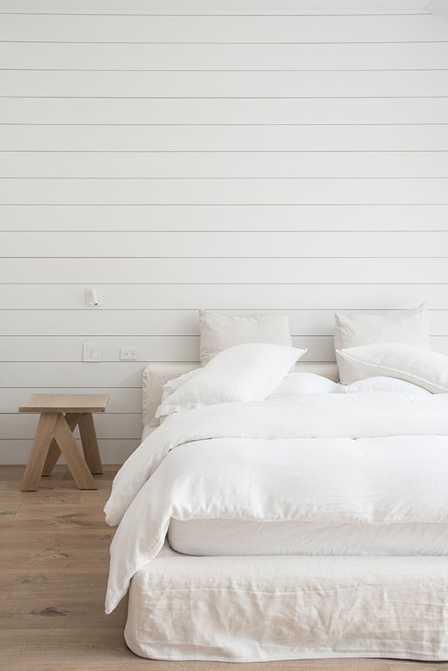 Dormitorio con sabanas blancas y taburete de madera