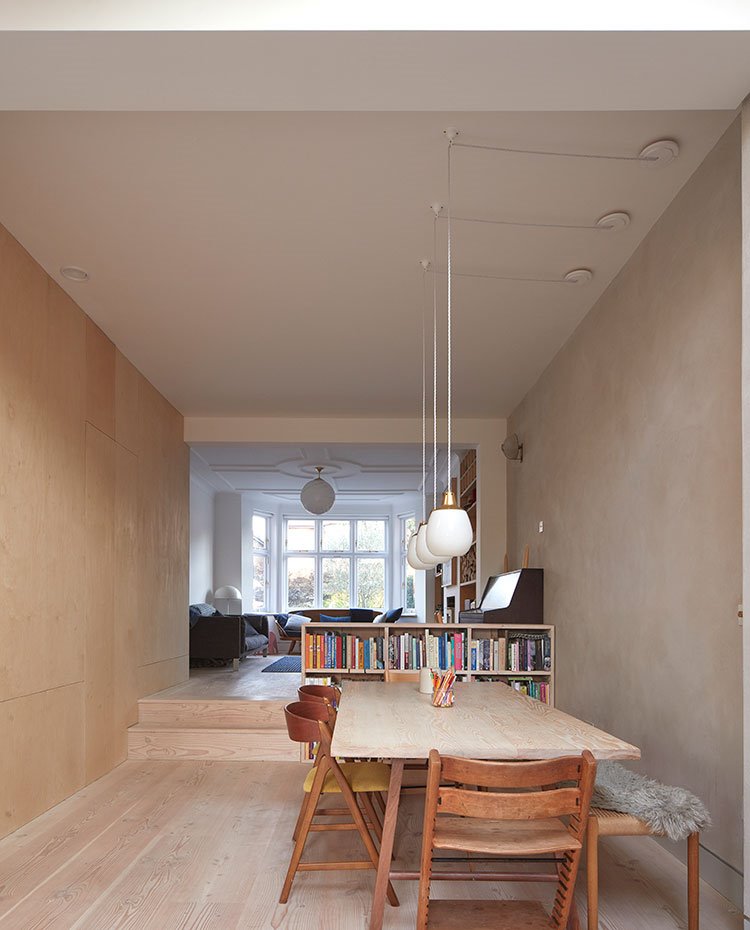 Luminarias suspendidas sobre mesa de comedor bajo techo de gran altura, esntante separador a modo de librería junto a escalones que conducen a zona de estar