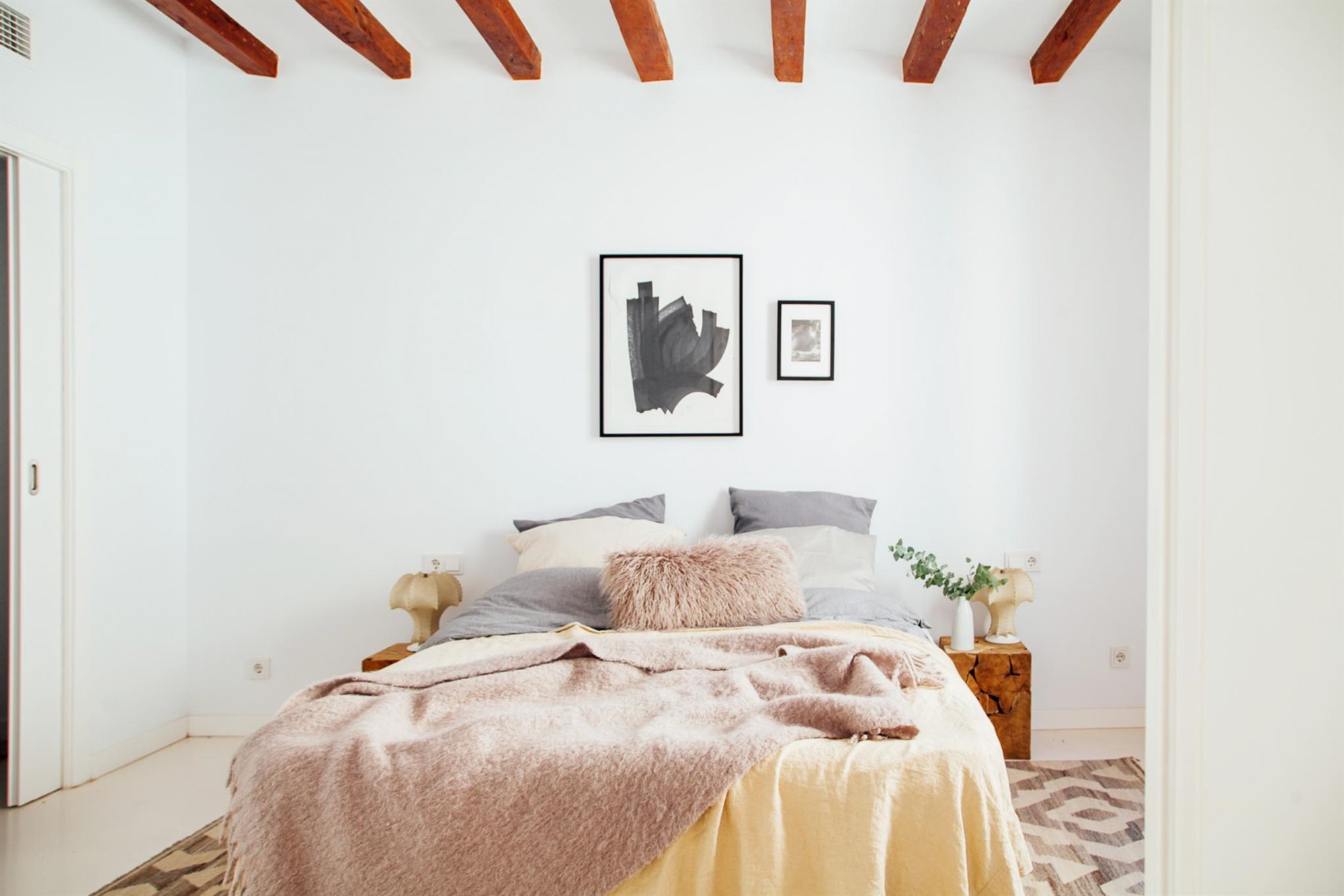 Dormitorio con ropa de cama natural y vigas vistas. Tejidos naturales
