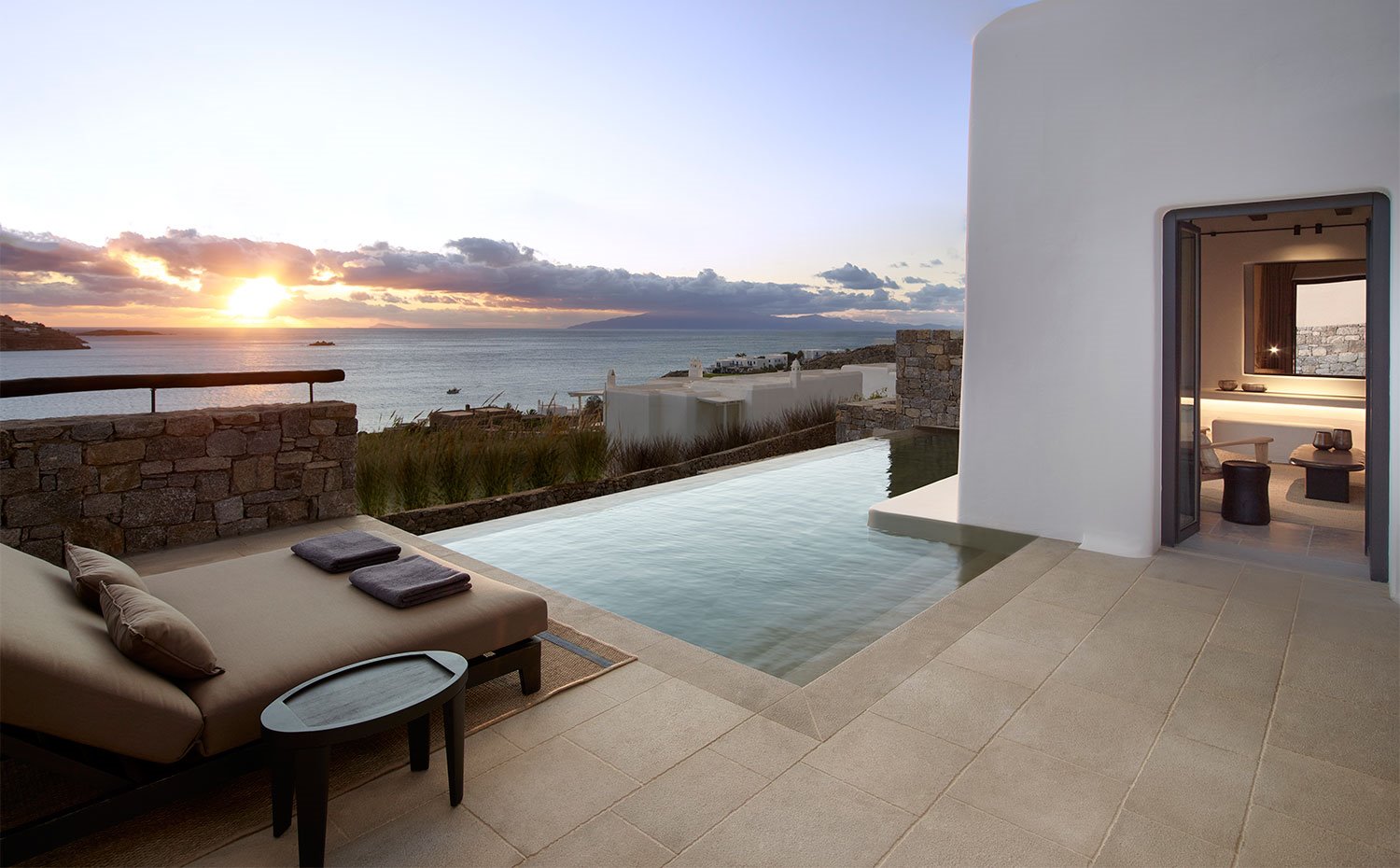 Vista de la terraza con tumbona y mesilla auxiliar junto a piscina infinita y vistas al mar