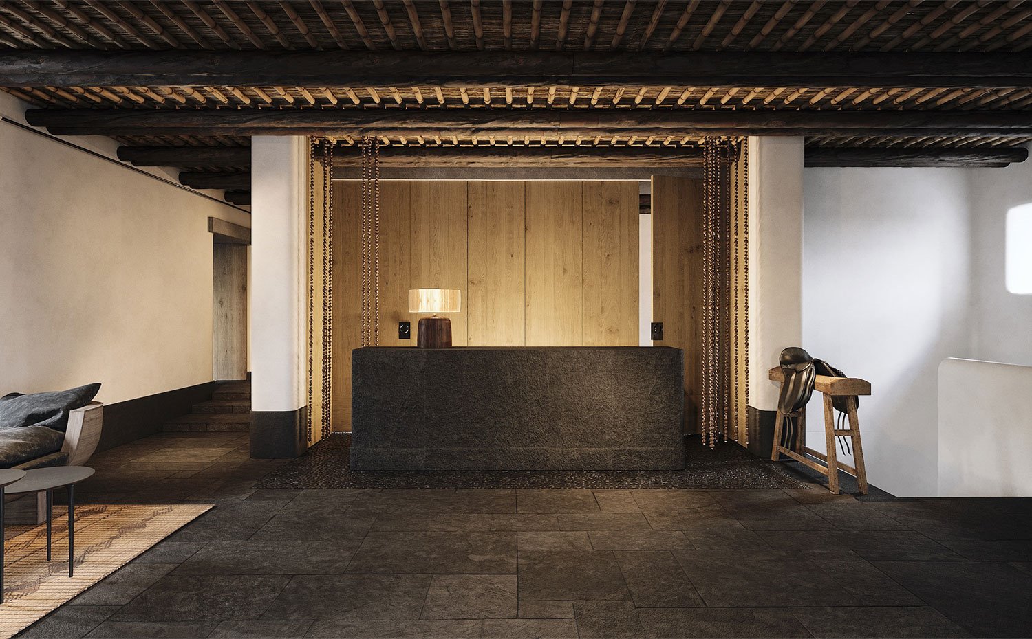 Zona de recepción de hotel con suelo y mostrados en piedra oscura, luminaria de sobremesa cálida, vigas de madera y cubierta de paja