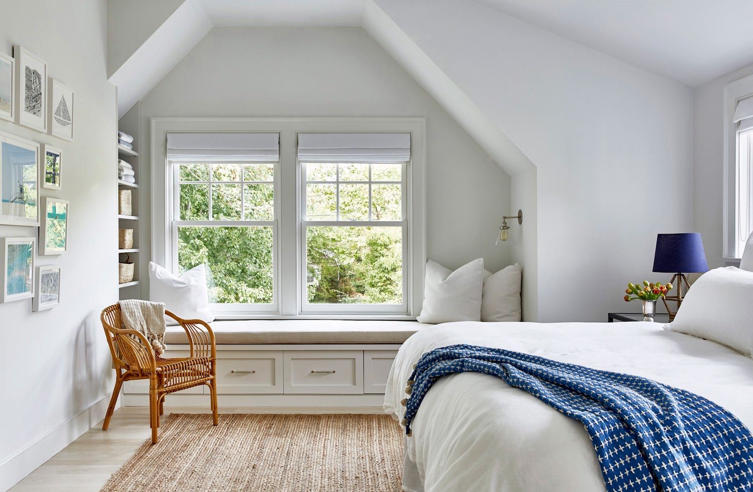 Dormitorio blanco con silla de mimbre y ropa de cama azul y blanca