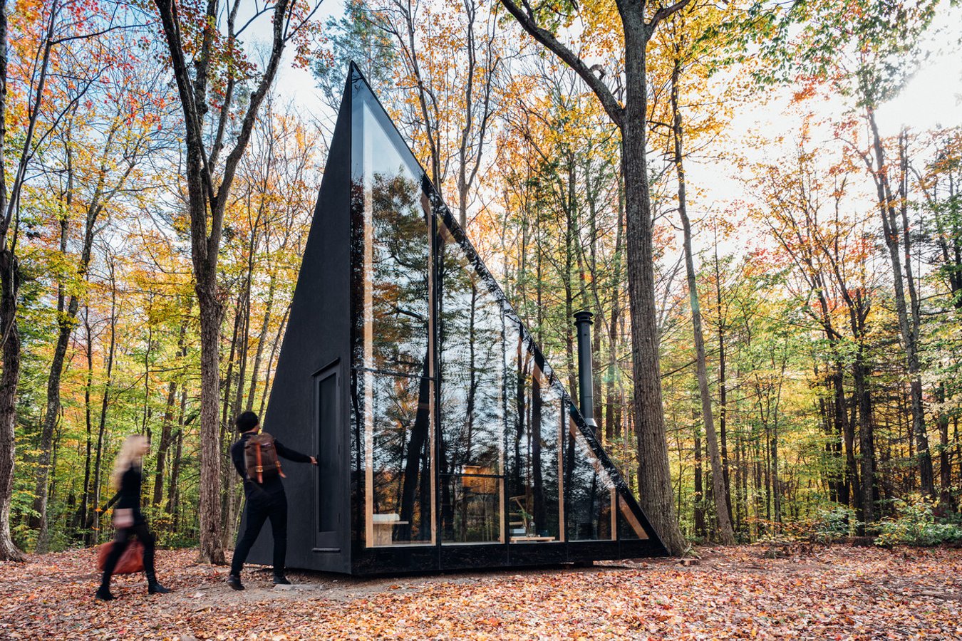 Cabaña con diseño triangular con una fachada de vidrio en medio del bosque.