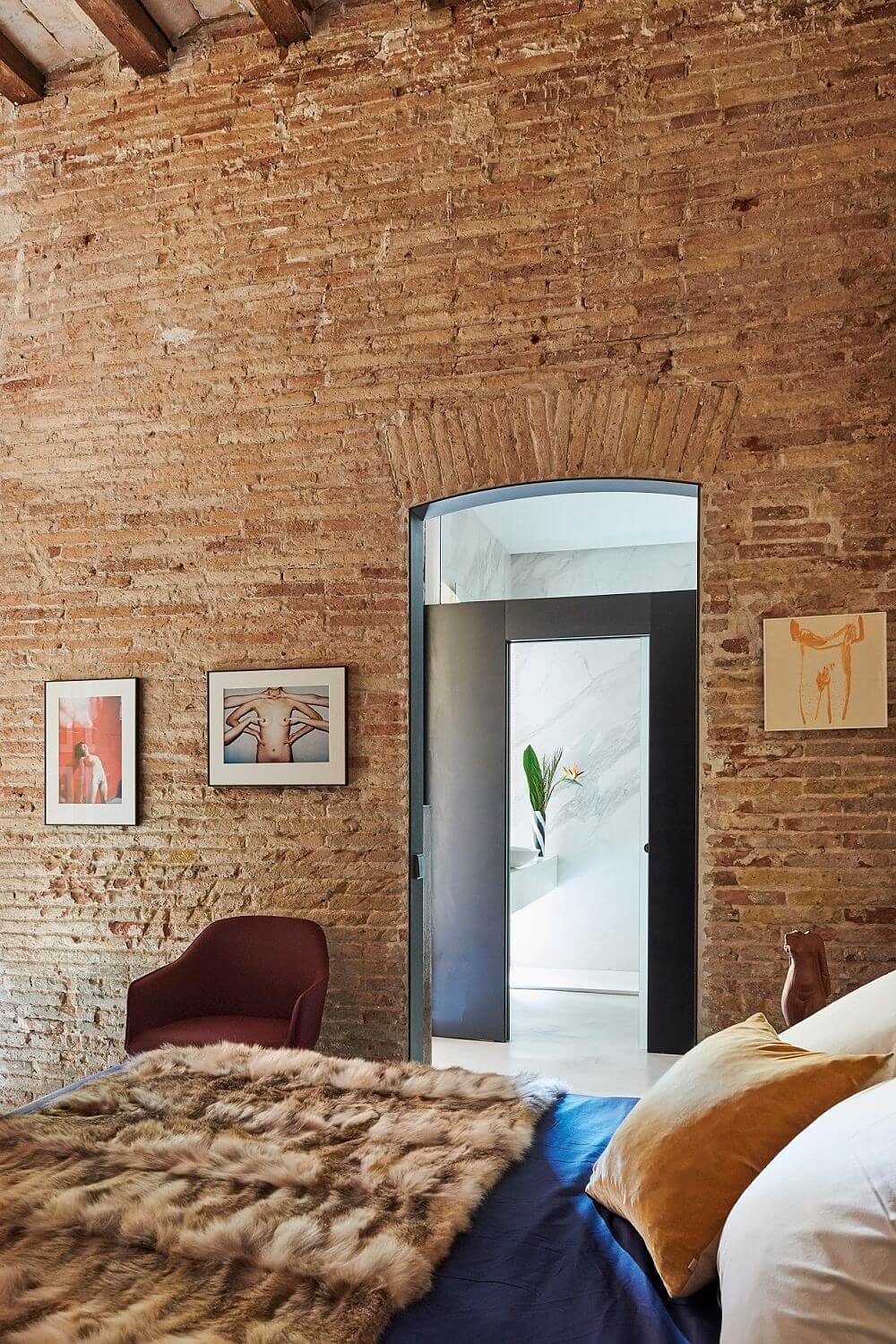 Dormitorio con paredes de ladrillo y butaca de cuero.
