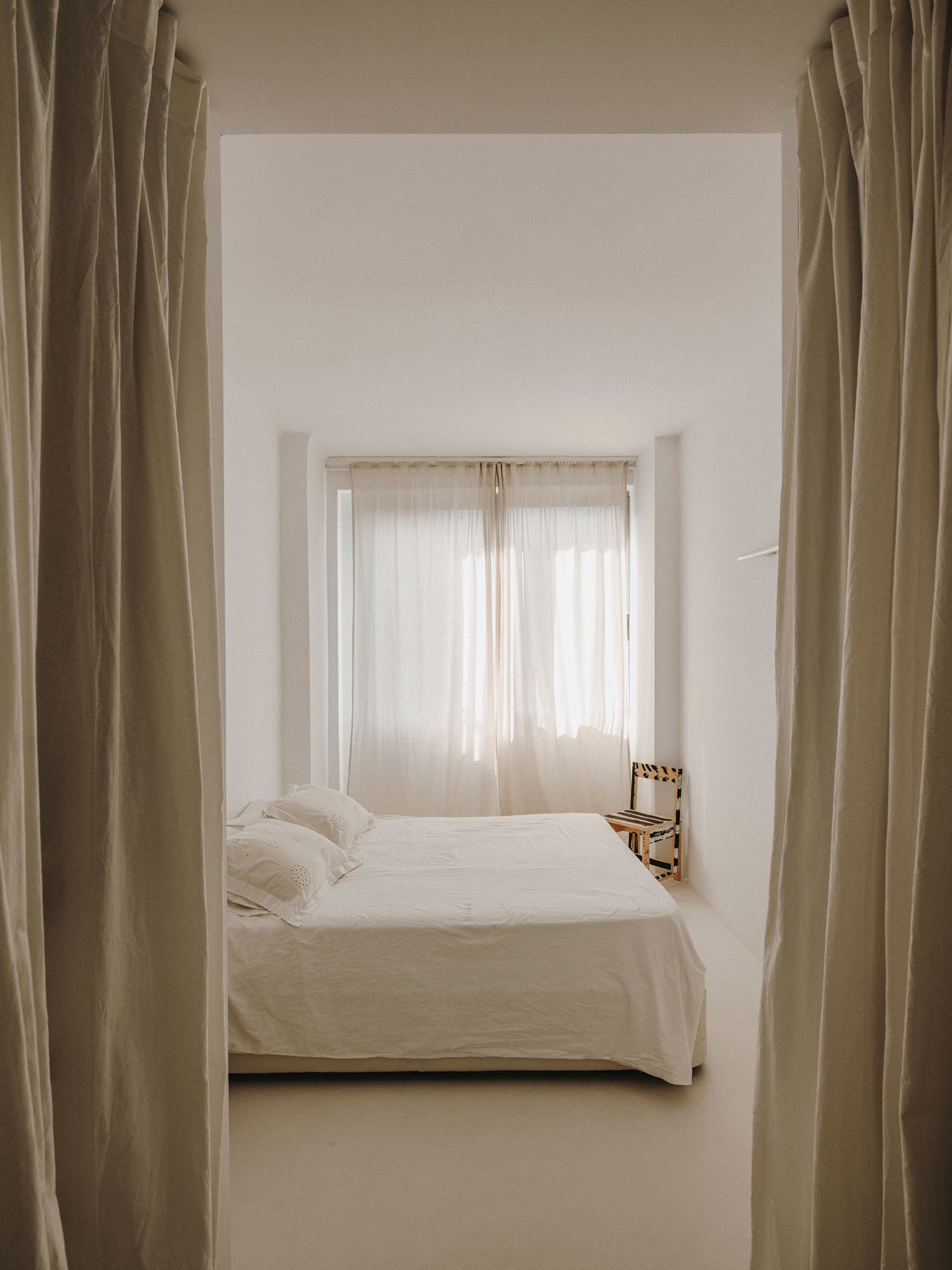 dormitorio en tonos claros con cama con ropa de cama blanca y cortinas color crema