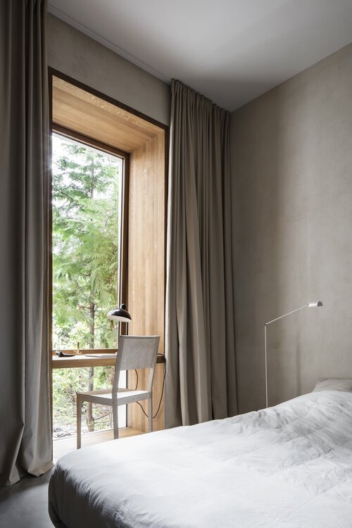 Dormitorio de estilo nórdico con silla y  escritorio que da a la ventana.