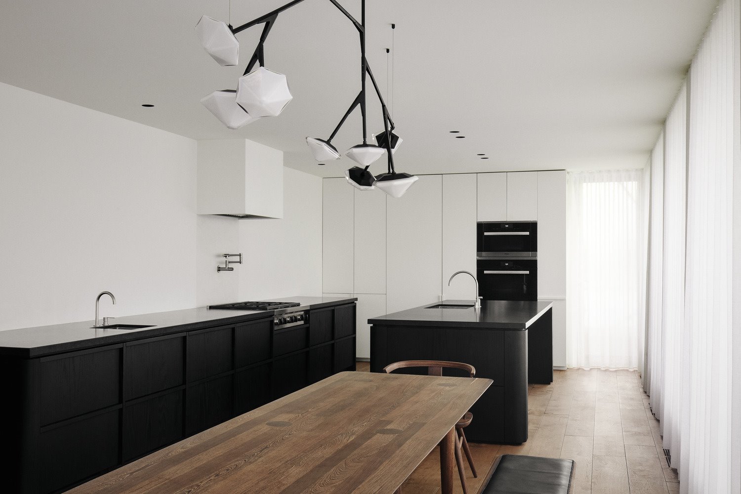 Cocina moderna con muebles blancos, isla negra y mesa de madera.