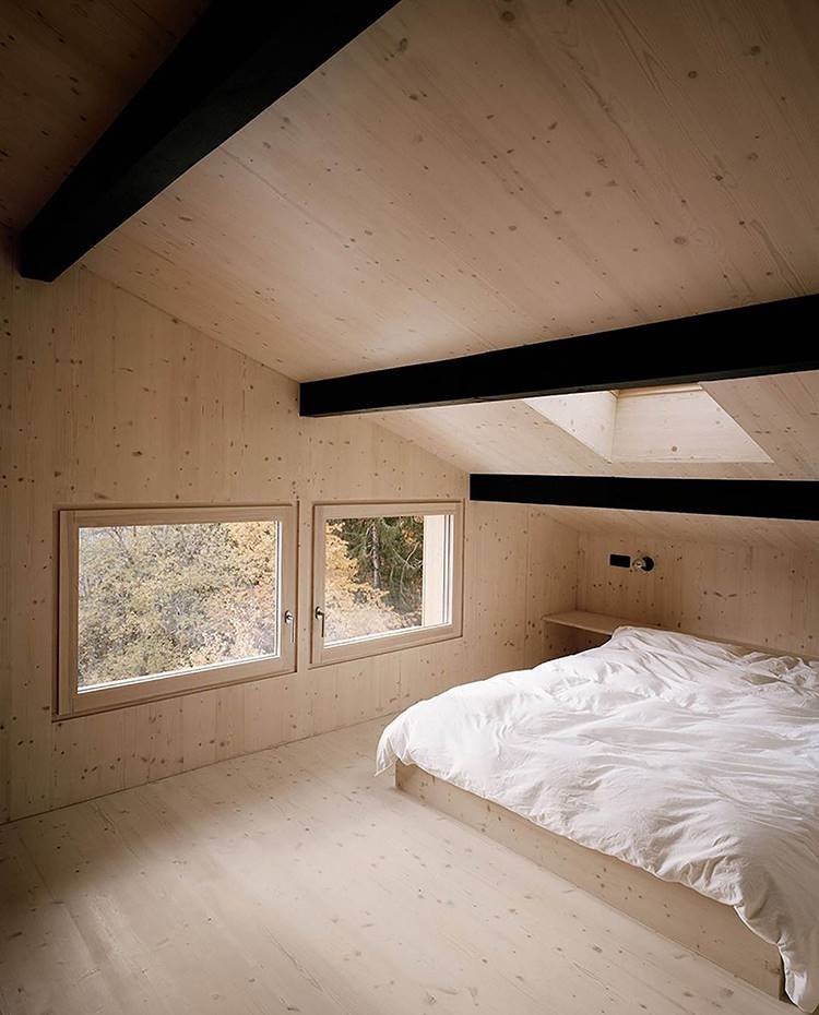 Dormitorio con techo abuhardillado, revestido con madera y ventana en el techo.