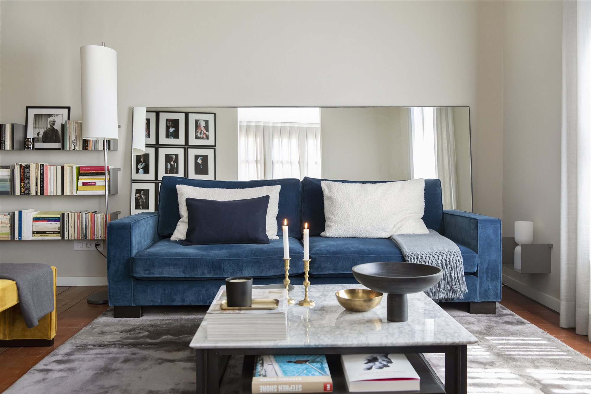 Salón con sofá azul y espejo sin marco detrás.