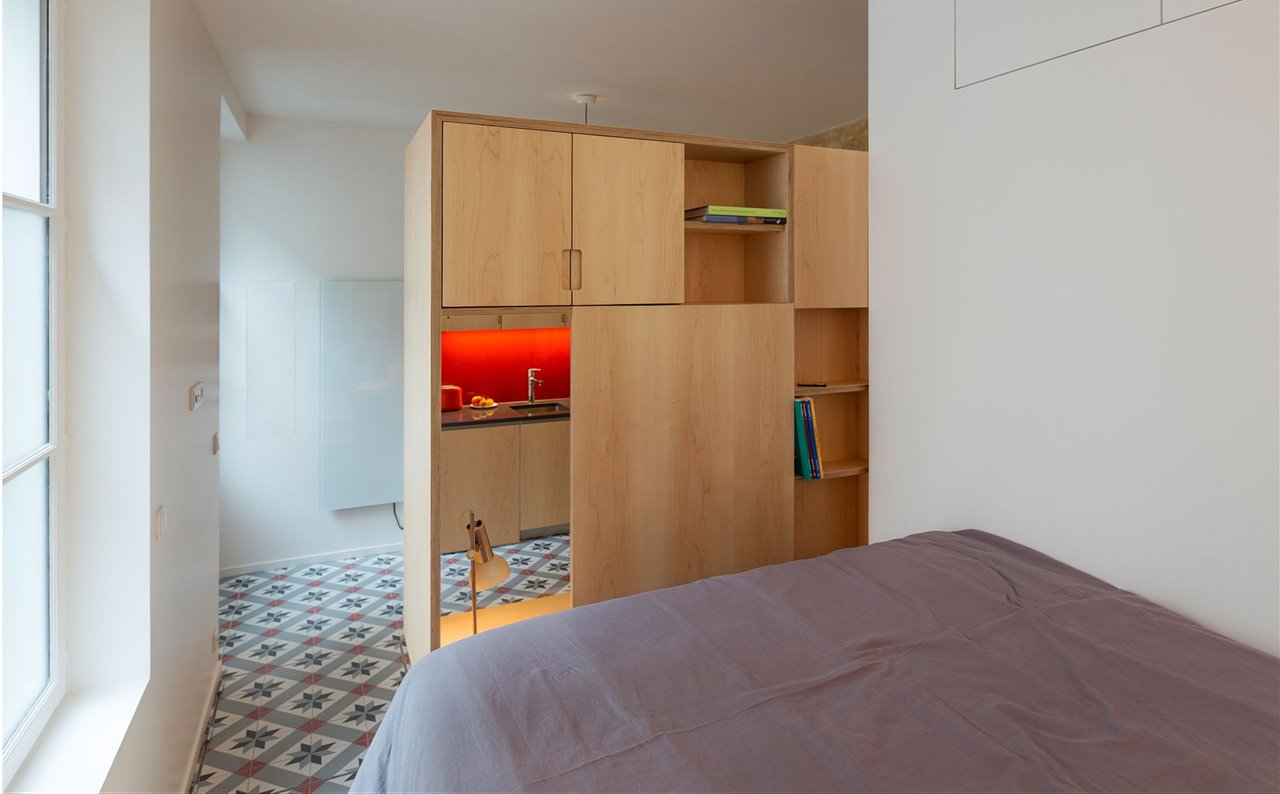 Un mueble multifuncional de madera nórdica efectúa la transición entre los dos espacios. Aunque la cama es de grandes proporciones, no se percibe como un elemento pesado.