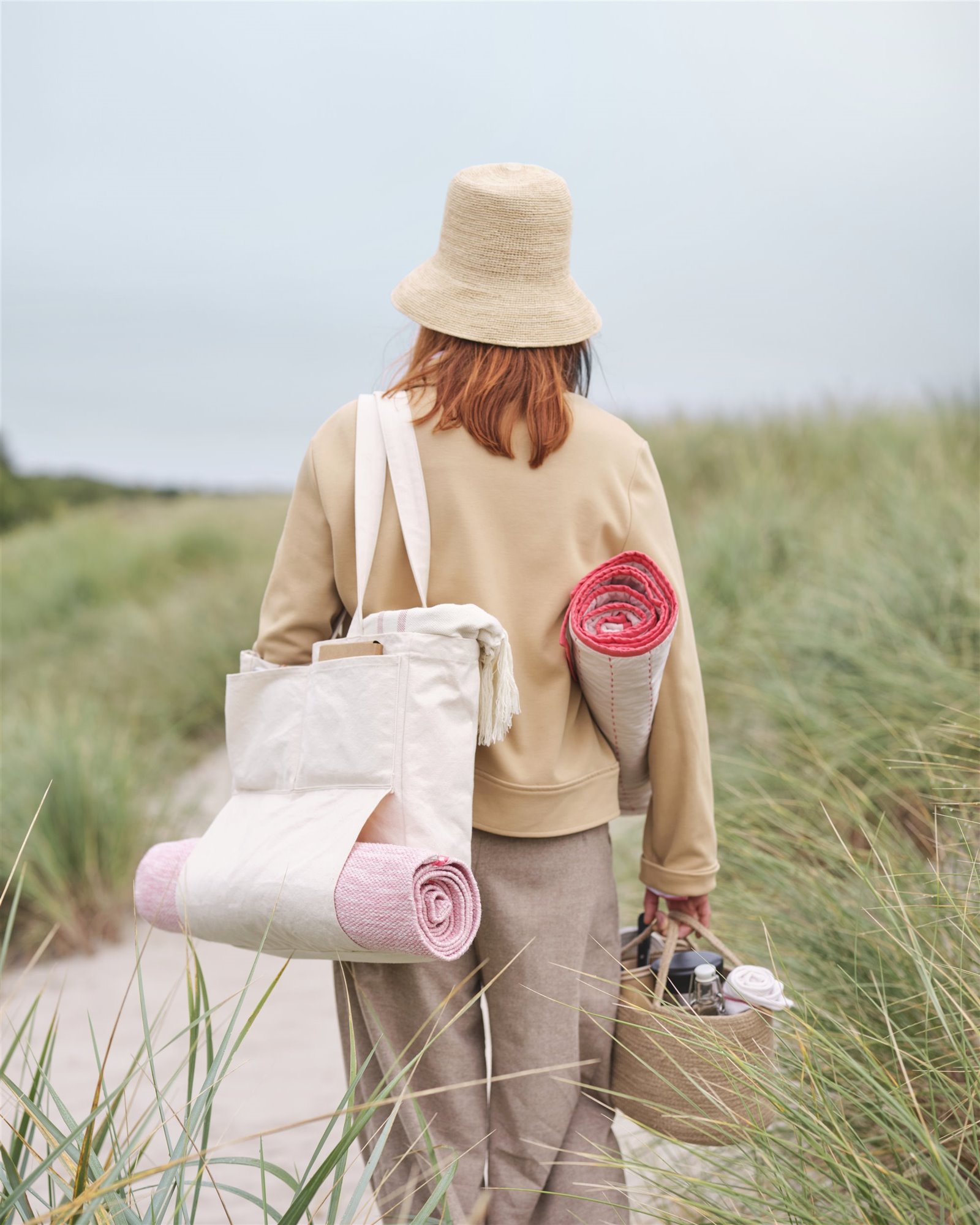 mujer en el campo con una bolsa de tela, esterilla, manta y cesta de mimbre de picinic