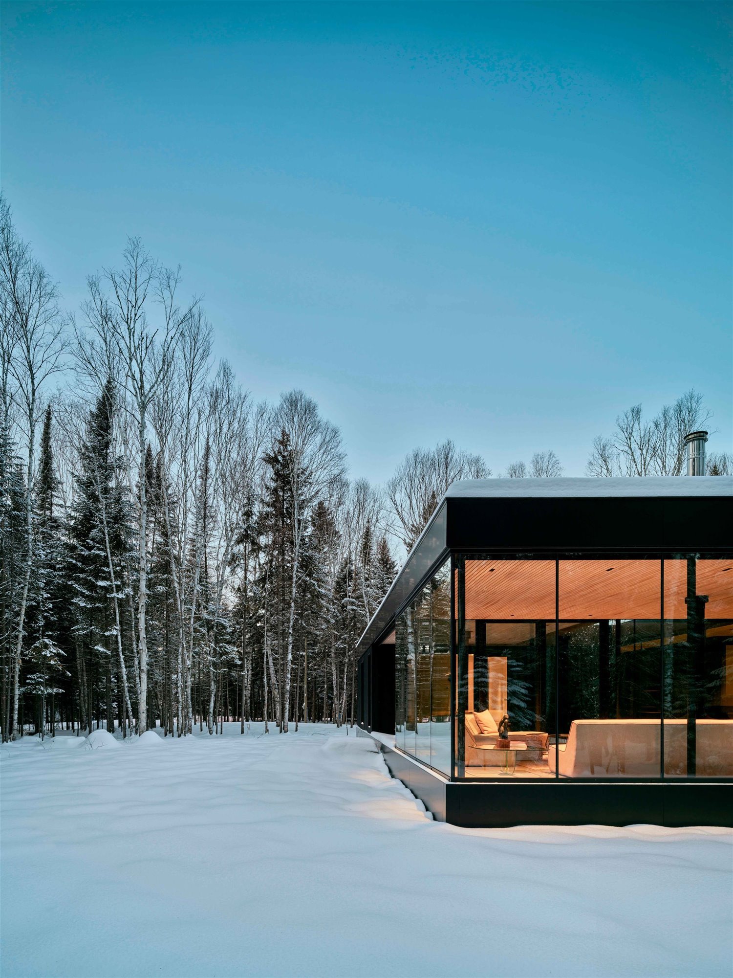 Fachada de una casa con ventanales de cristal en un paisaje nevado.
