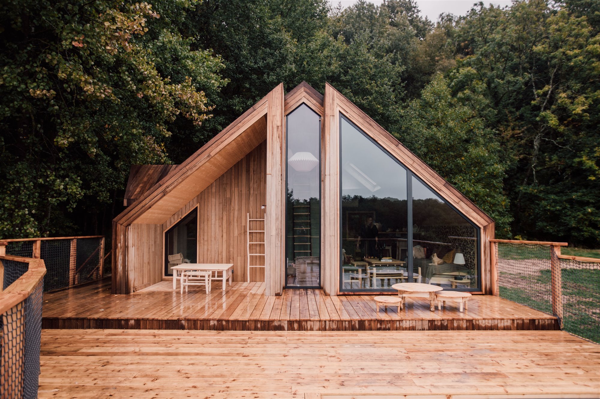 Cabaña de madera de forma triangular con grandes ventanas.