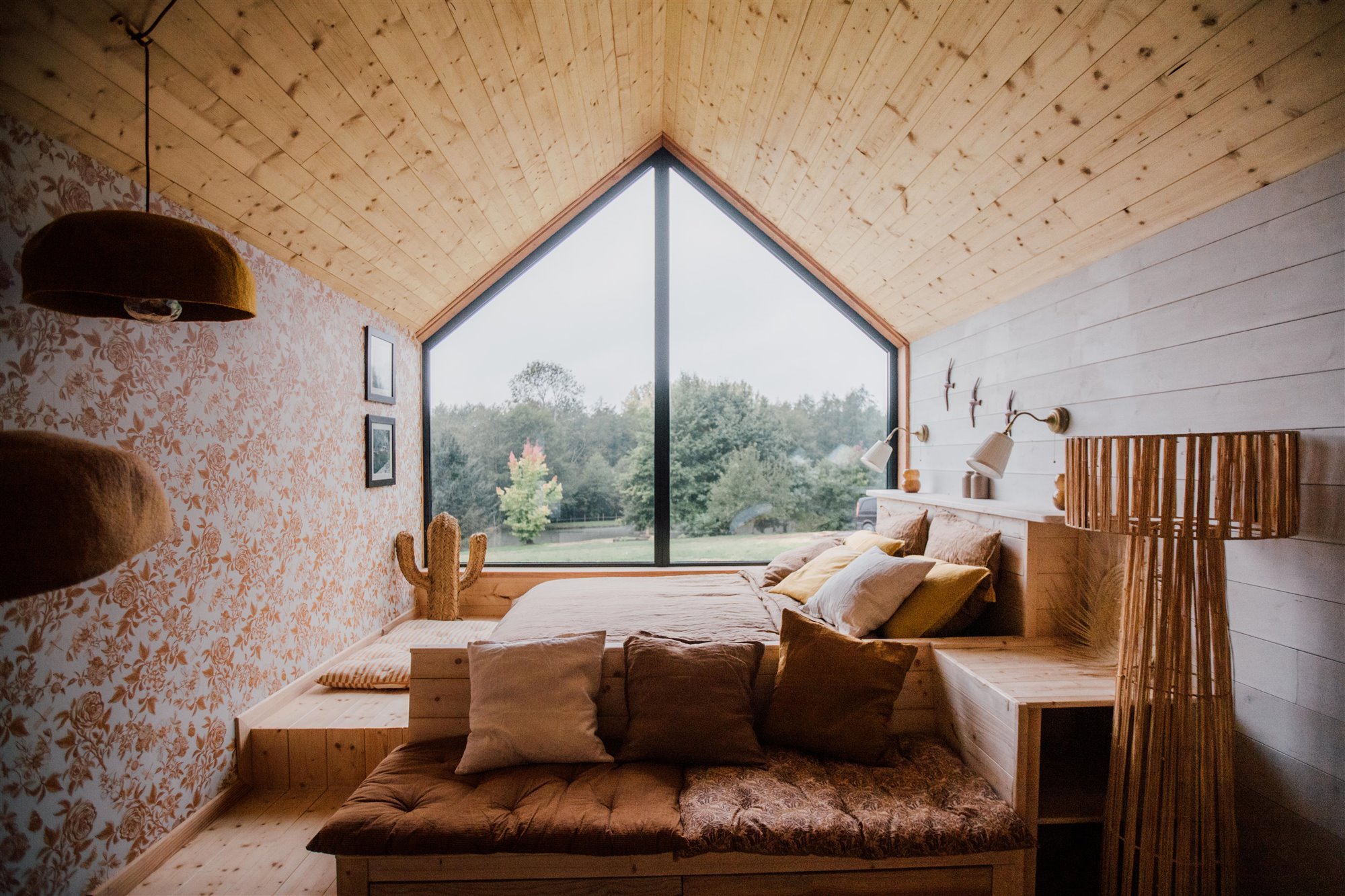 Dormitorio revestido de madera y papel pintado con cama de obra de madera.