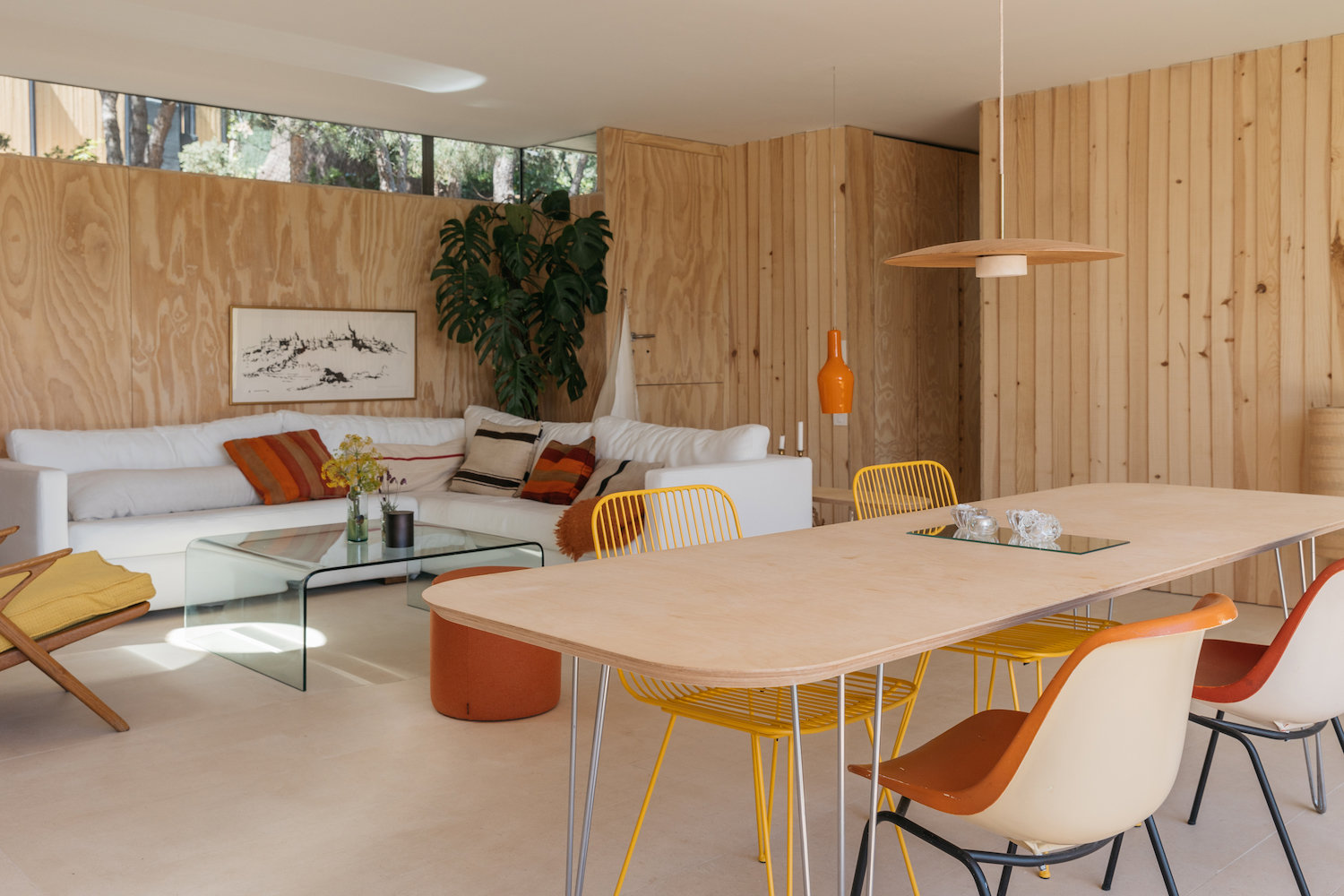 salón-comedor con paredes de madera, sofá blanco y mesa de madera con sillas de color amarillo.