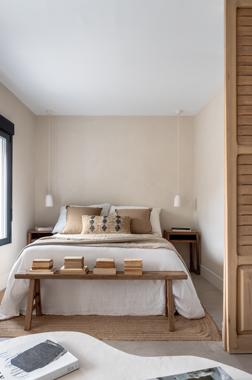 cama con ropa de cama de lino, un banco de madera y plaid de color arena