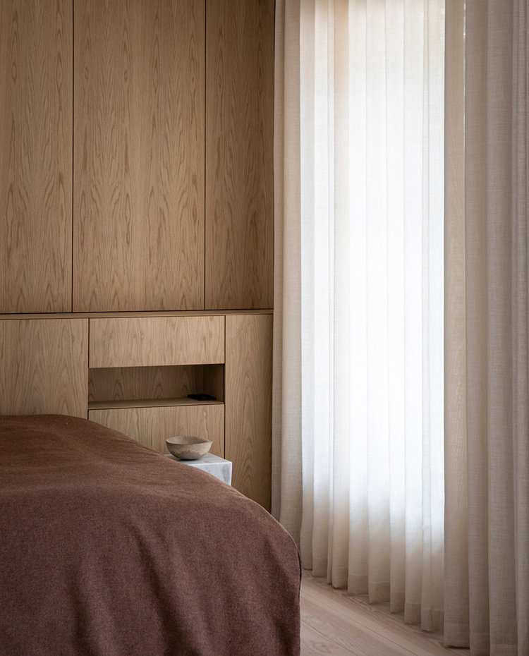 Dormitorio con mobiliario de madera personalizado y cortinas blancas y crudas para las aperturas.