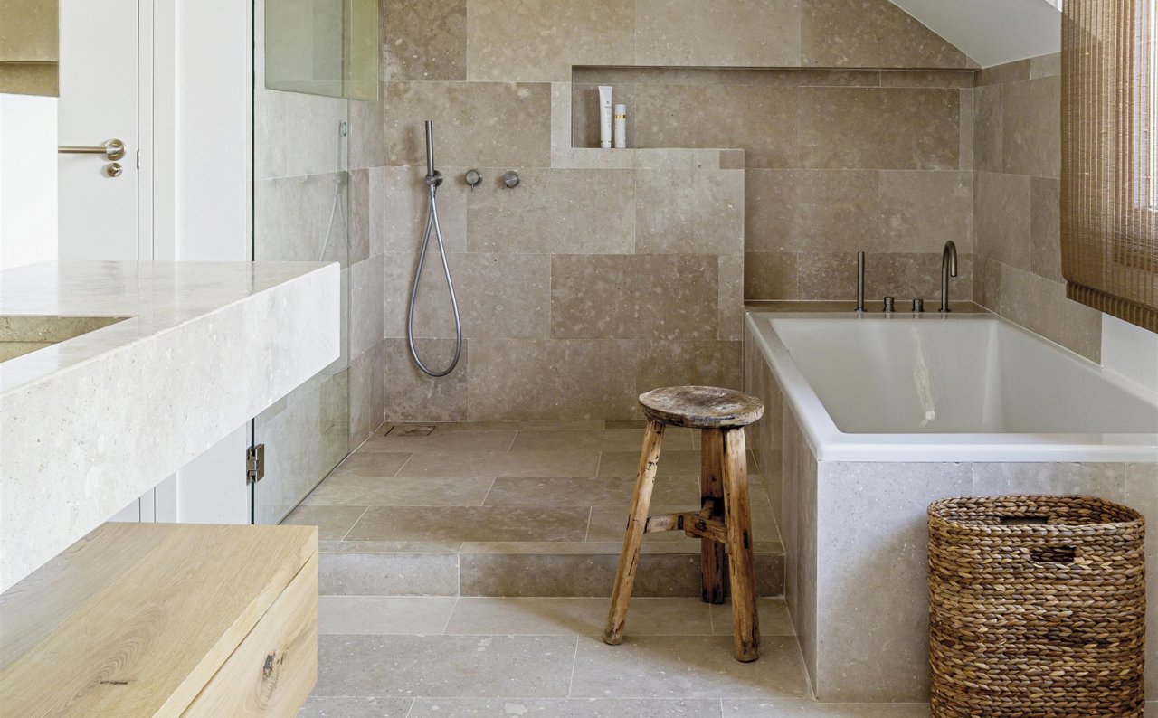 baño de piedra con bañera, cesto de mimbre y taburete de madera