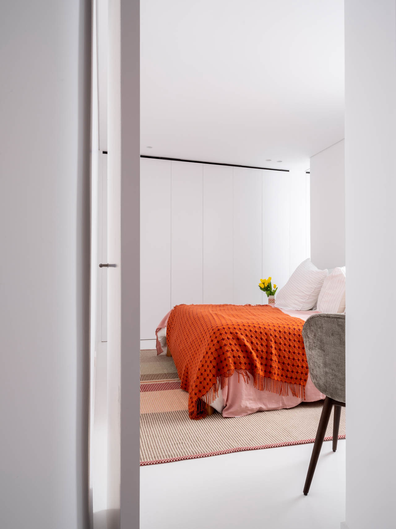 Dormitorio con armario empotrado blanco y colcha naranja.