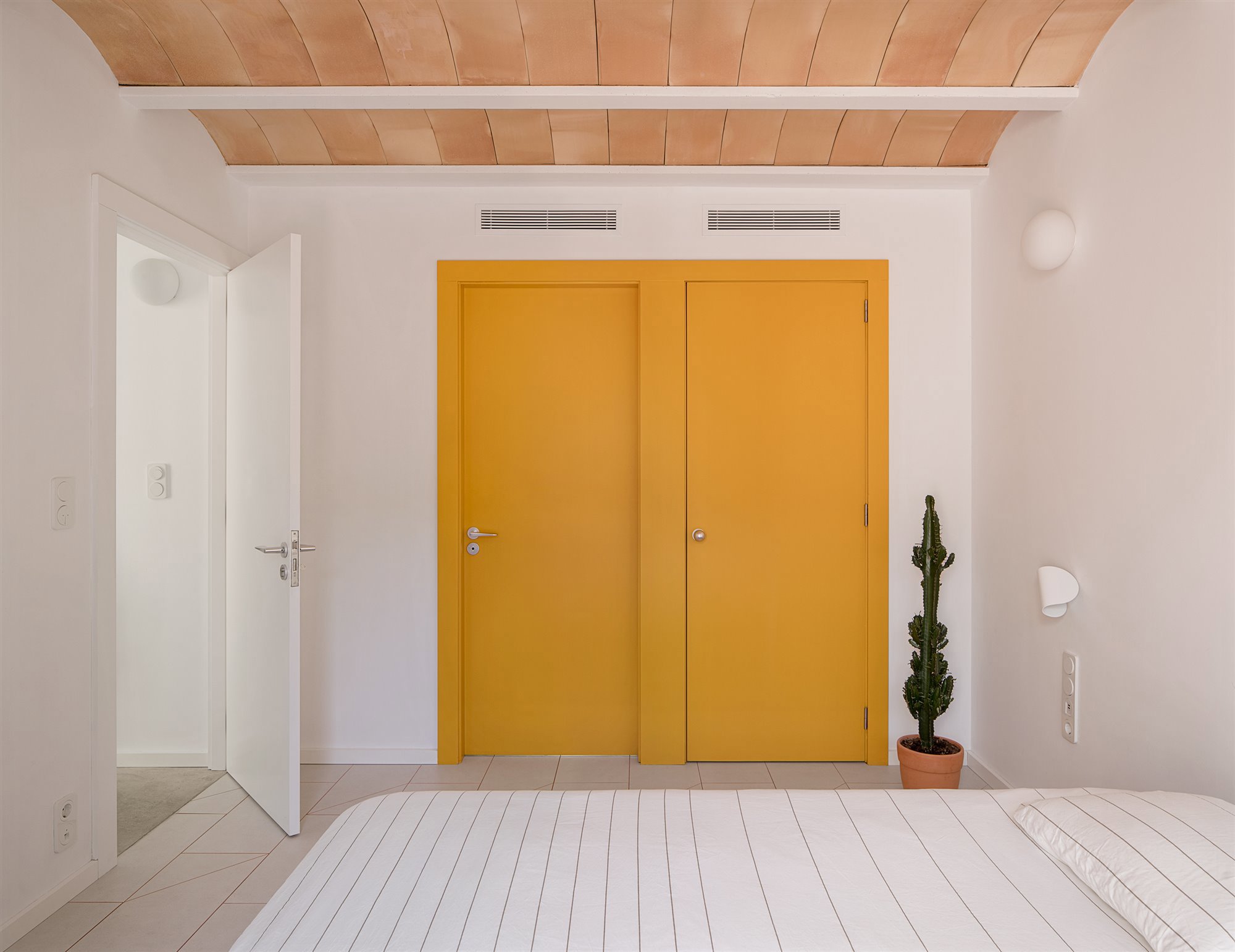 Un dormitorio acogedor en el que destaca el techo de bovedilla y el punto de color en amarillo.