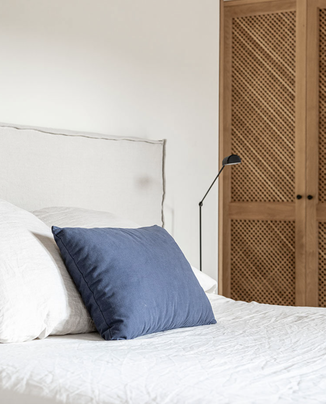 cama en blanco con cojin azul y armario de madera