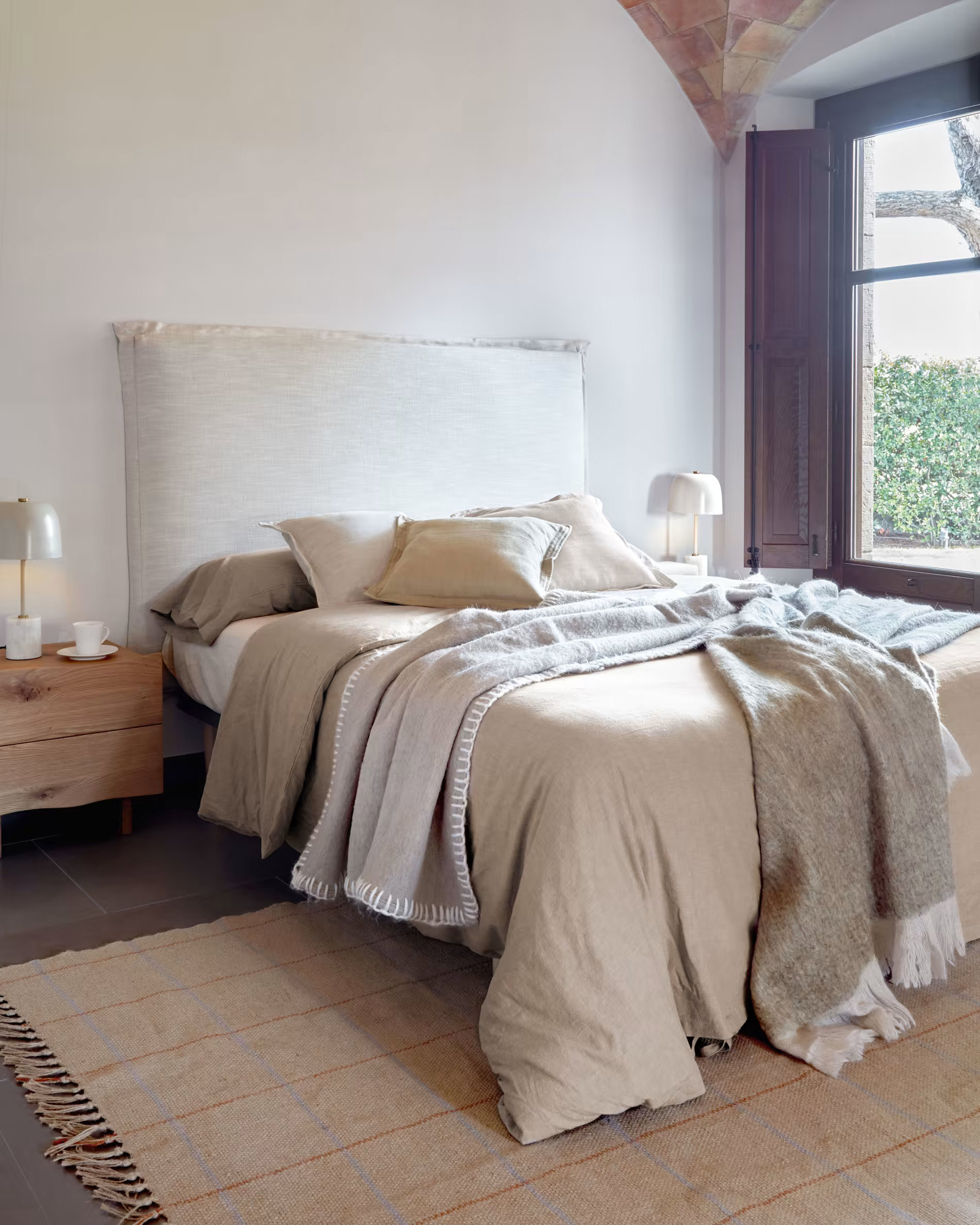Dormitorio con cabecero blanco y con mantas.