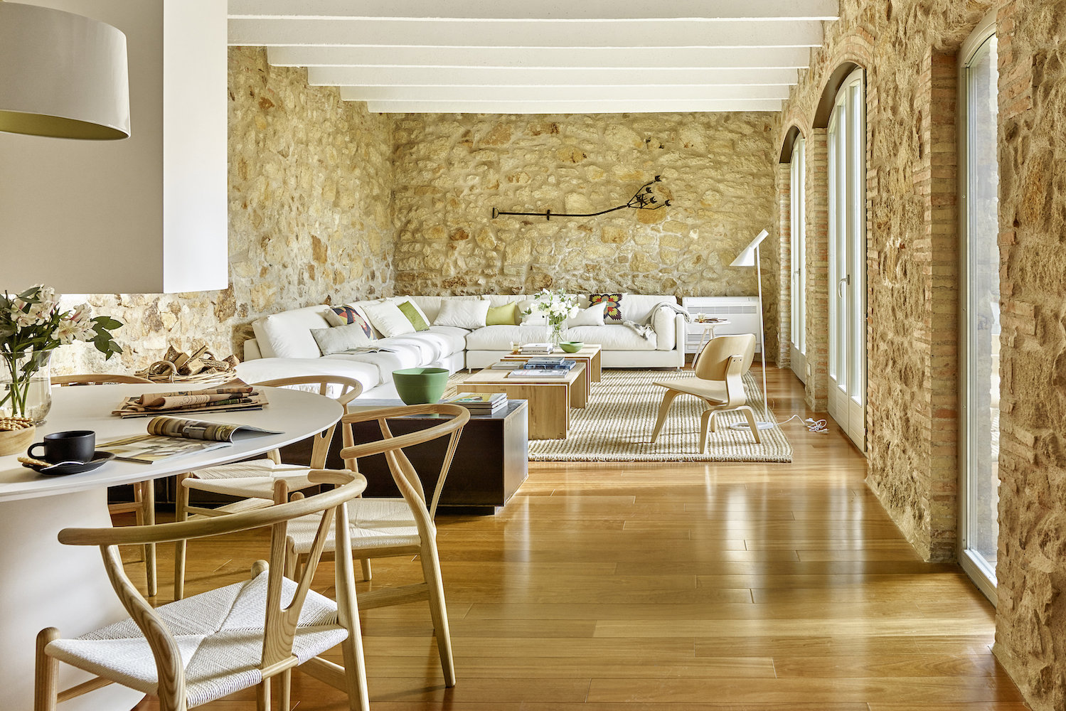 Casa moderna estilo rústico con salón y comedor con paredes de piedra y amplio sofá blanco en L.