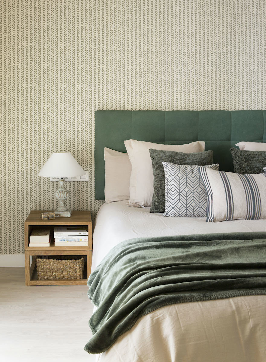 Dormitorio con cabecero tapizado y papel pintado floral.