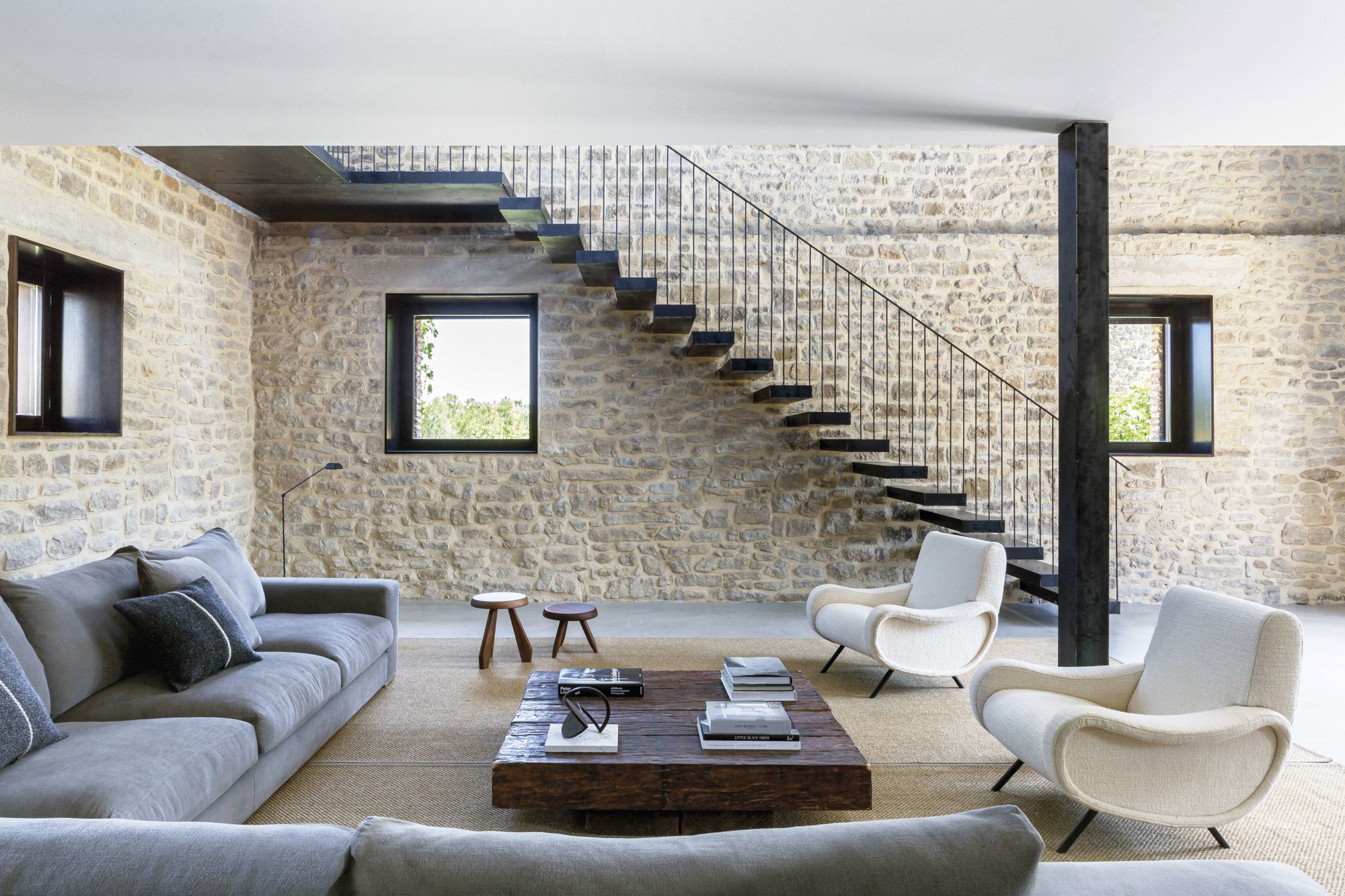 Salón con paredes de piedra, sofá XL y dos butacas blancas