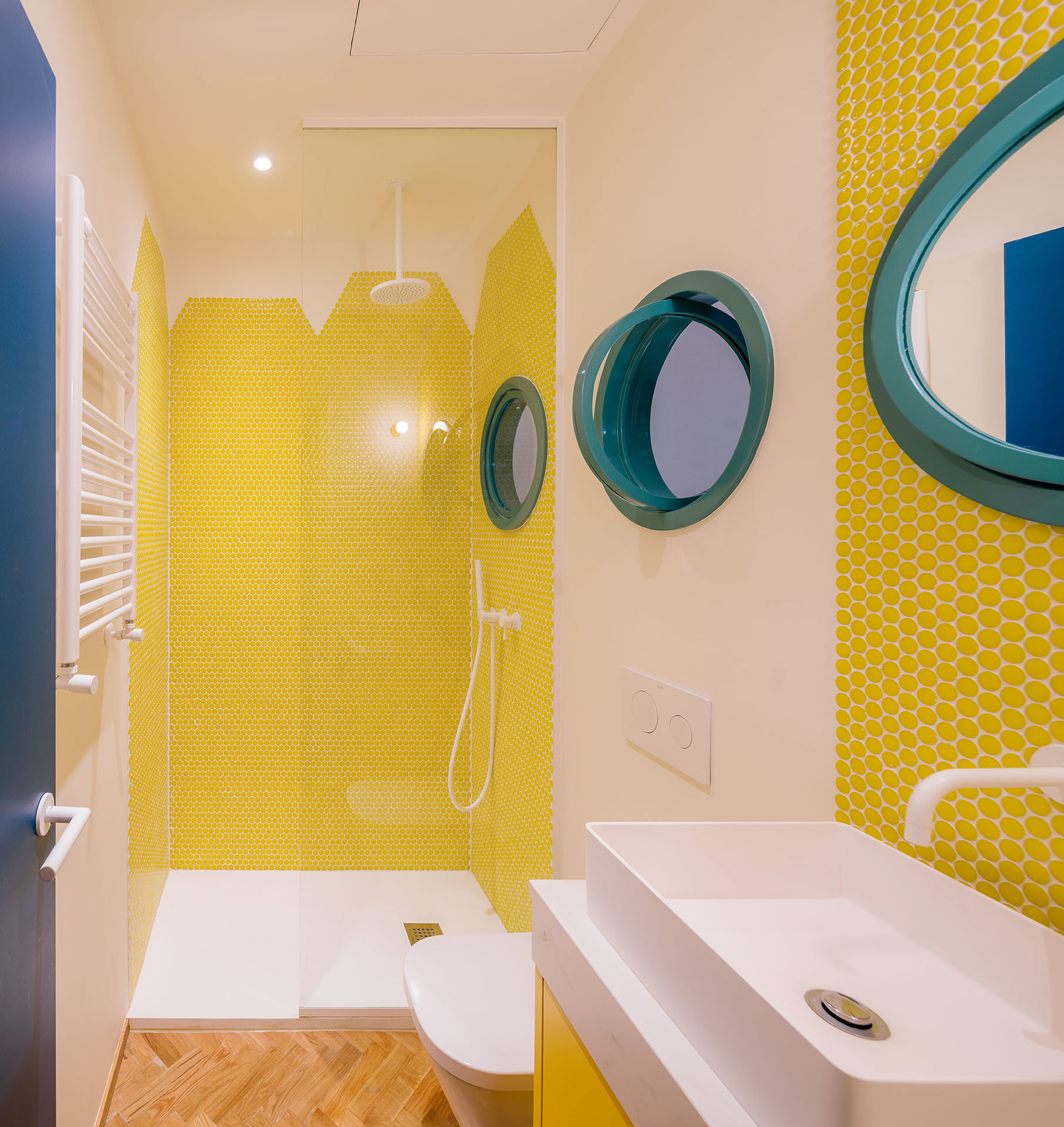 Baño con parees en amarillo y ventanas redondas con marco en azul turquesa.