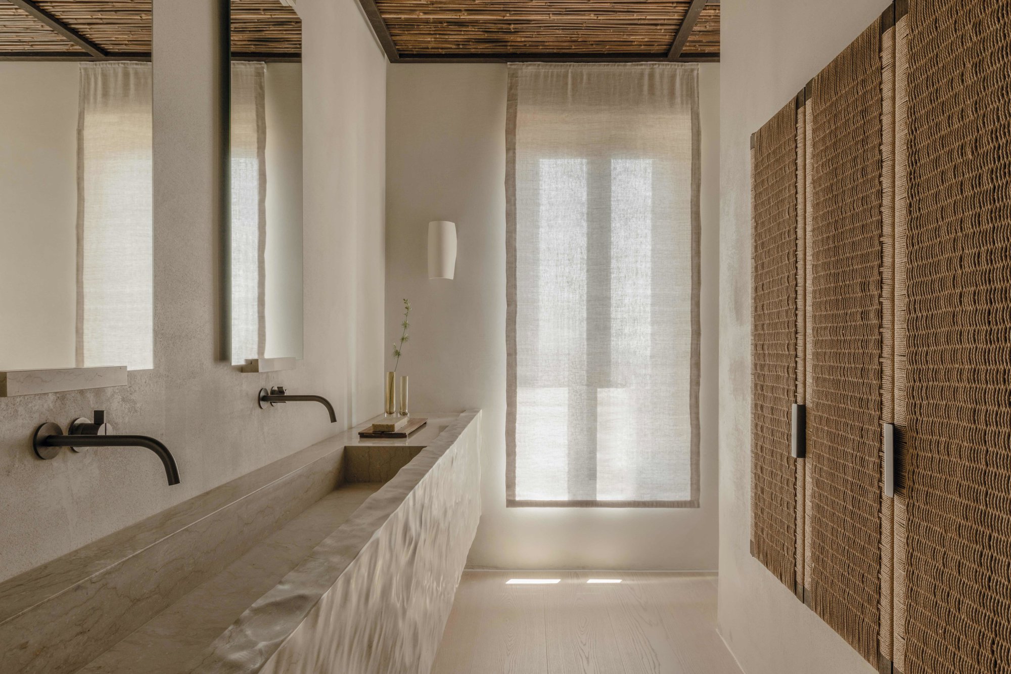 Baño con lavabo de piedra y armarios con puertas de fibra natural.