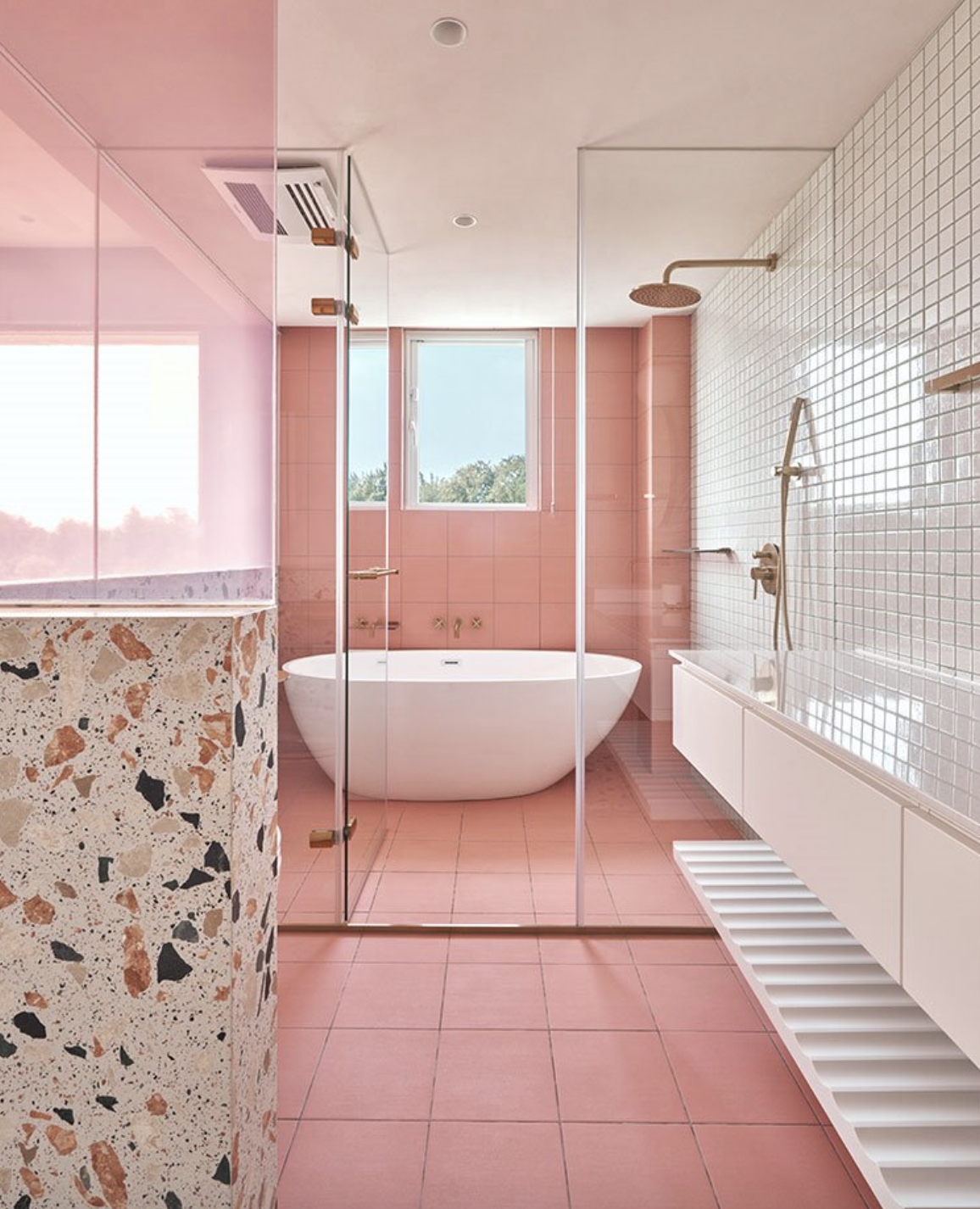 baño rosa con bañera exenta al fondo y azulejos blancos, rosas y terrazo