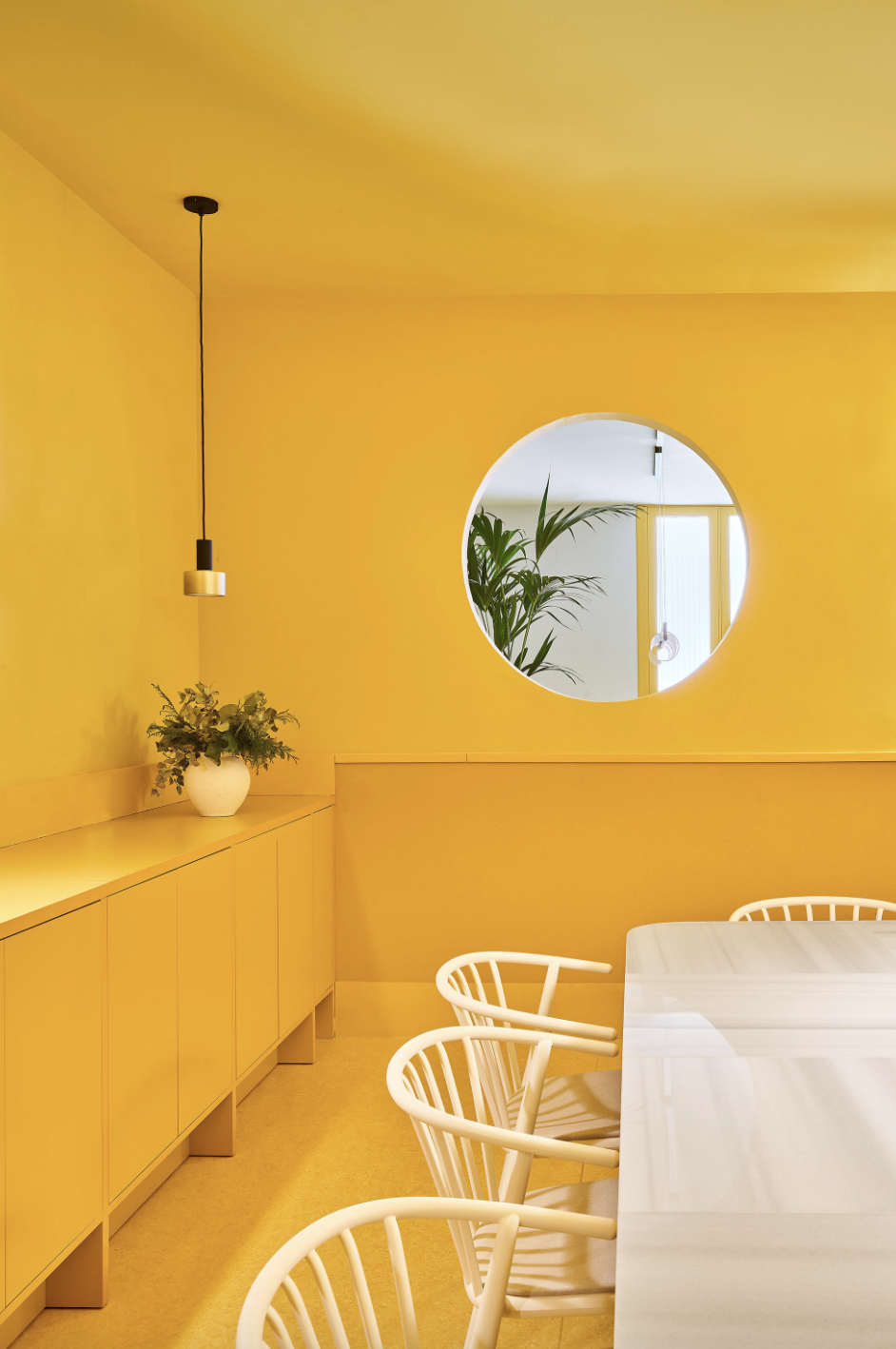 mesa de salón blanca con sillas de mimbre blancas y el resto, paredes y muebles, en amarillo, con una ventana redonda