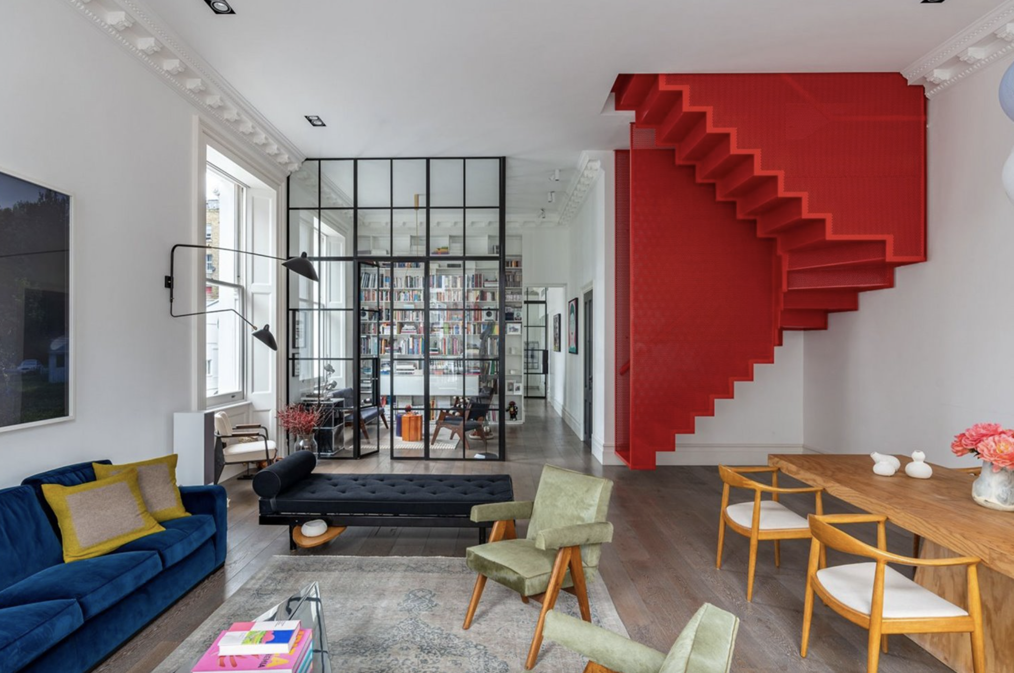salon con sofa azul, butacas verdes, una escalera roja y blanca y una puerta corredera de cristal con carpinteria negra