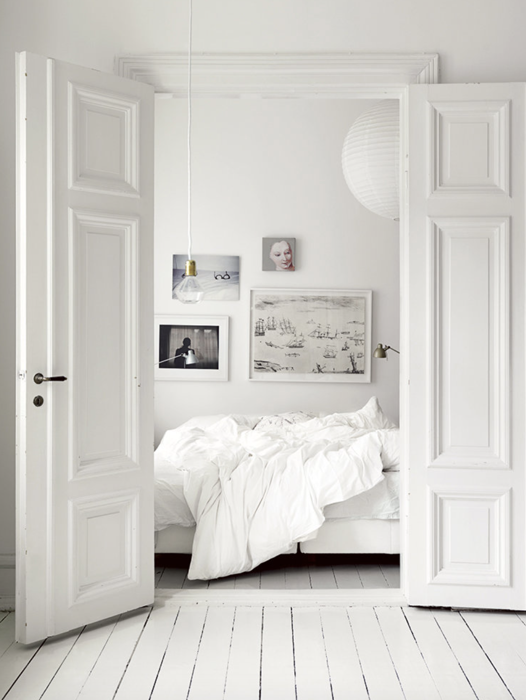 puertas abiertas en blanco que dan a un dormitorio blanco con cuadros en la pared