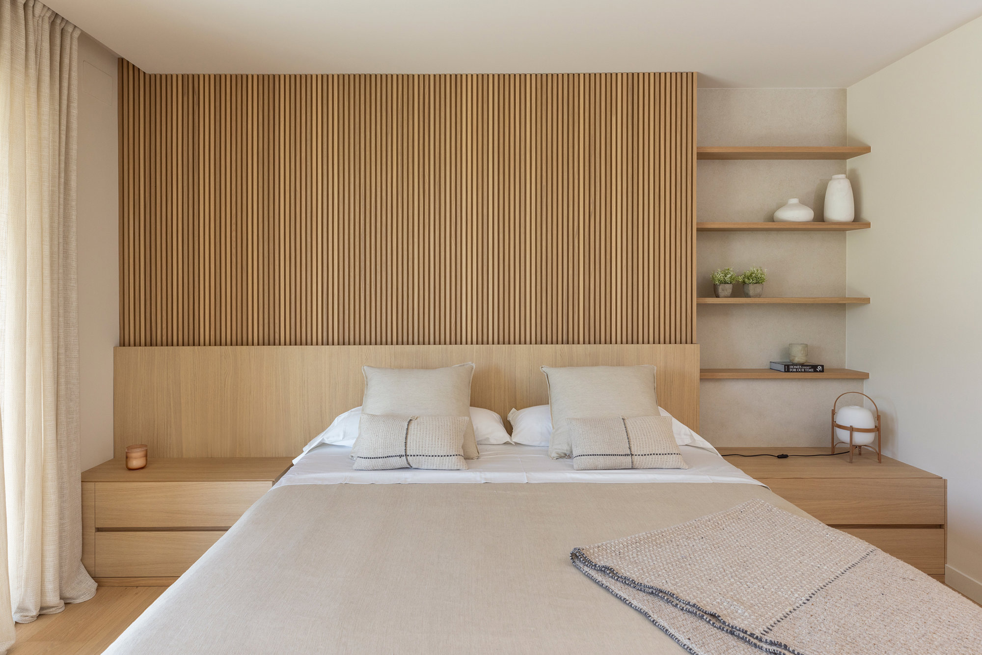 Dormitorio con cabecero de madera y mesitas y estantería integradas.