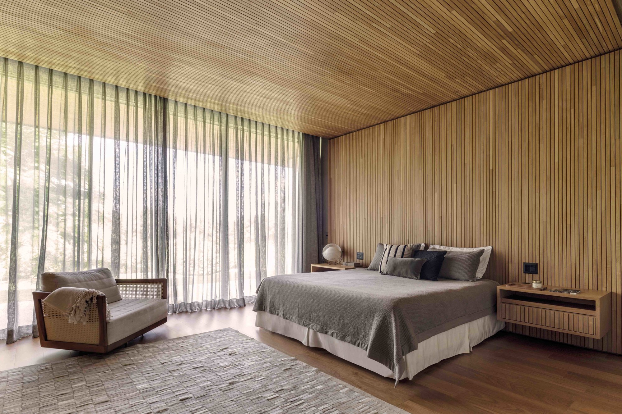 Dormitotorio con paredes, suelos y techos de madera y ropa de cama en blanco y gris.