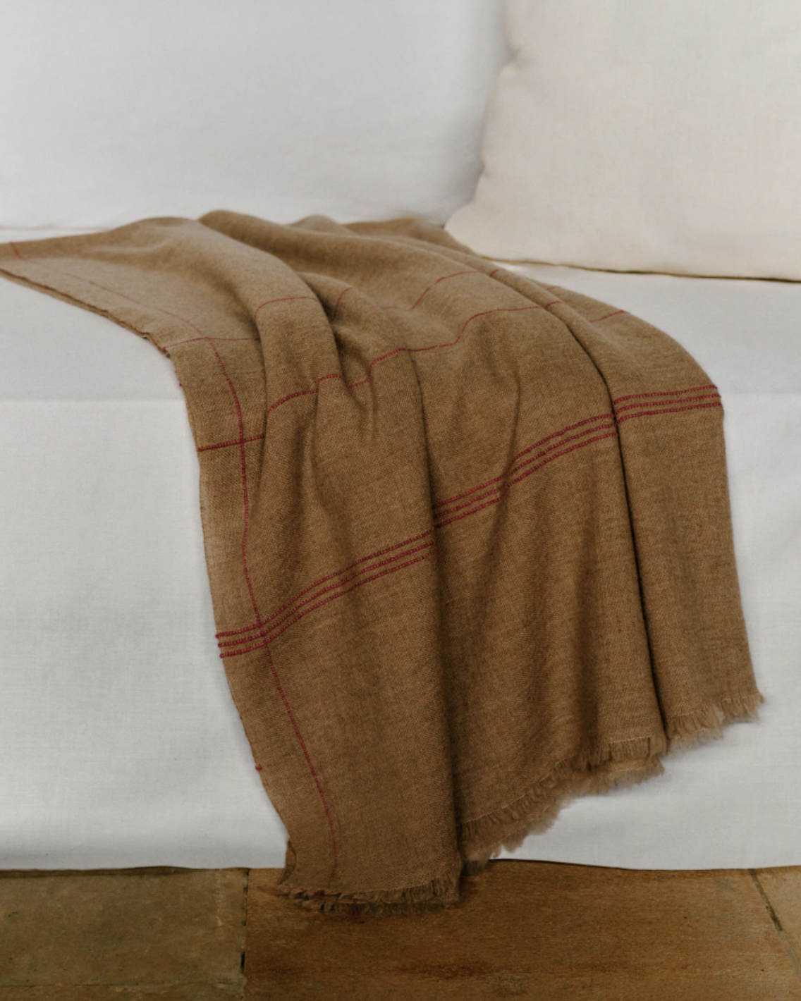 manta marrón con finas rayas rojas sobre una cama de colores blancos