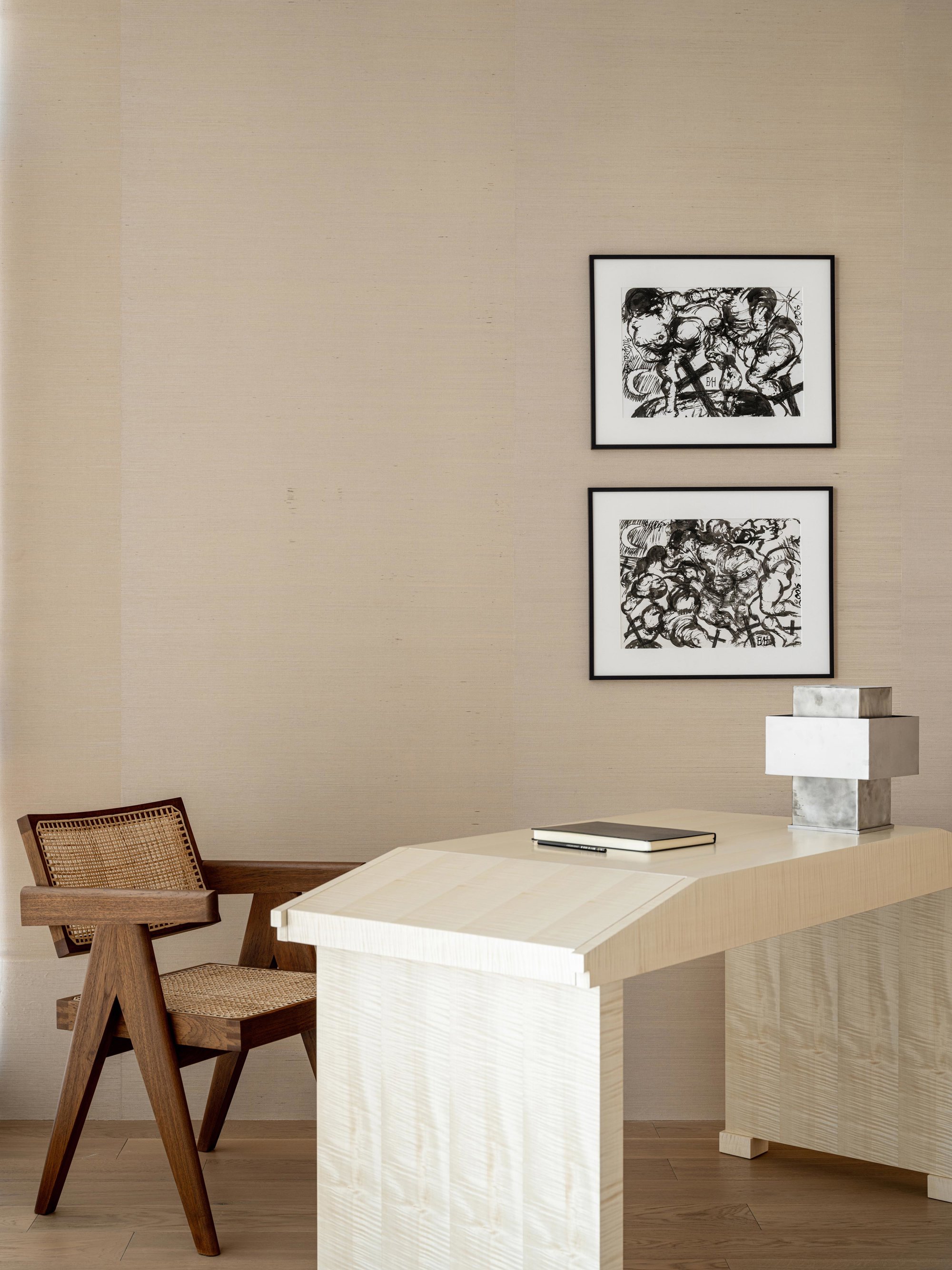 mesa de trabajo en blanco, con dos cuadros, una lampara en forma de cruz y una silla de mimbre