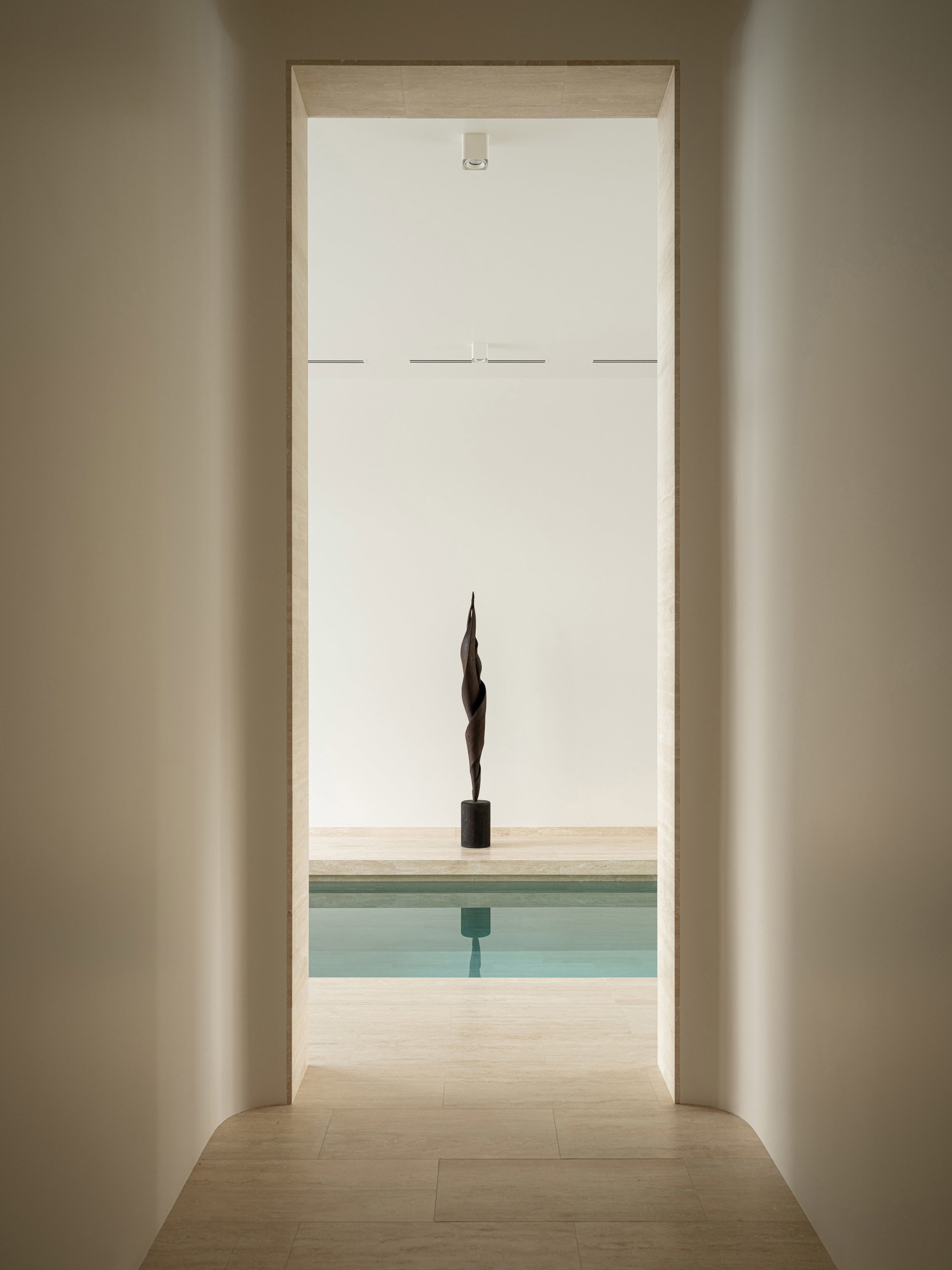 pasillo hacia una piscina con una escultura al fondo