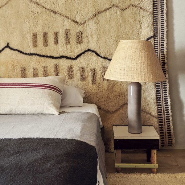 dormitorio con cabecero de lana, mesilla de madera, lámpara de cerámica y cama