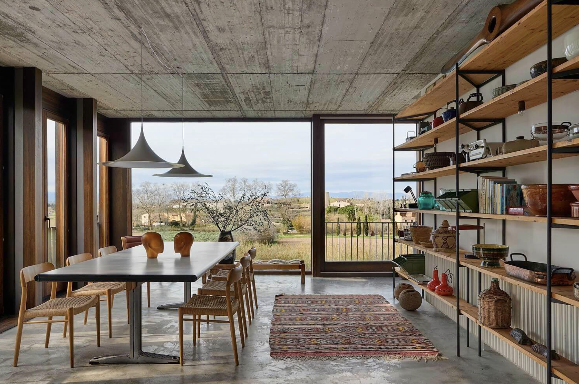 espacio con libreria, mesa de comedor, sillas, gran ventanal y techo de hormigon