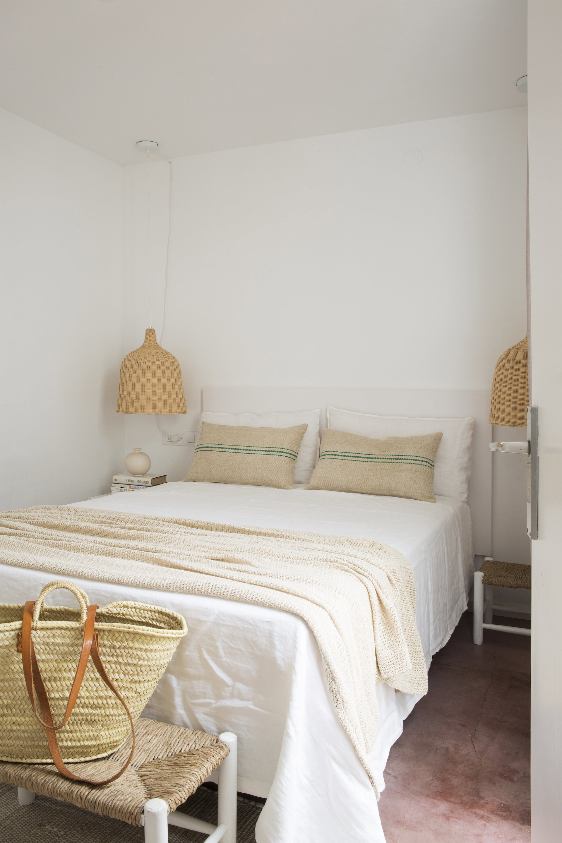 Dormitorio minimalista en blanco con tonos cálidos en los cojines, las lámparas, la ropa de cama y el taburete