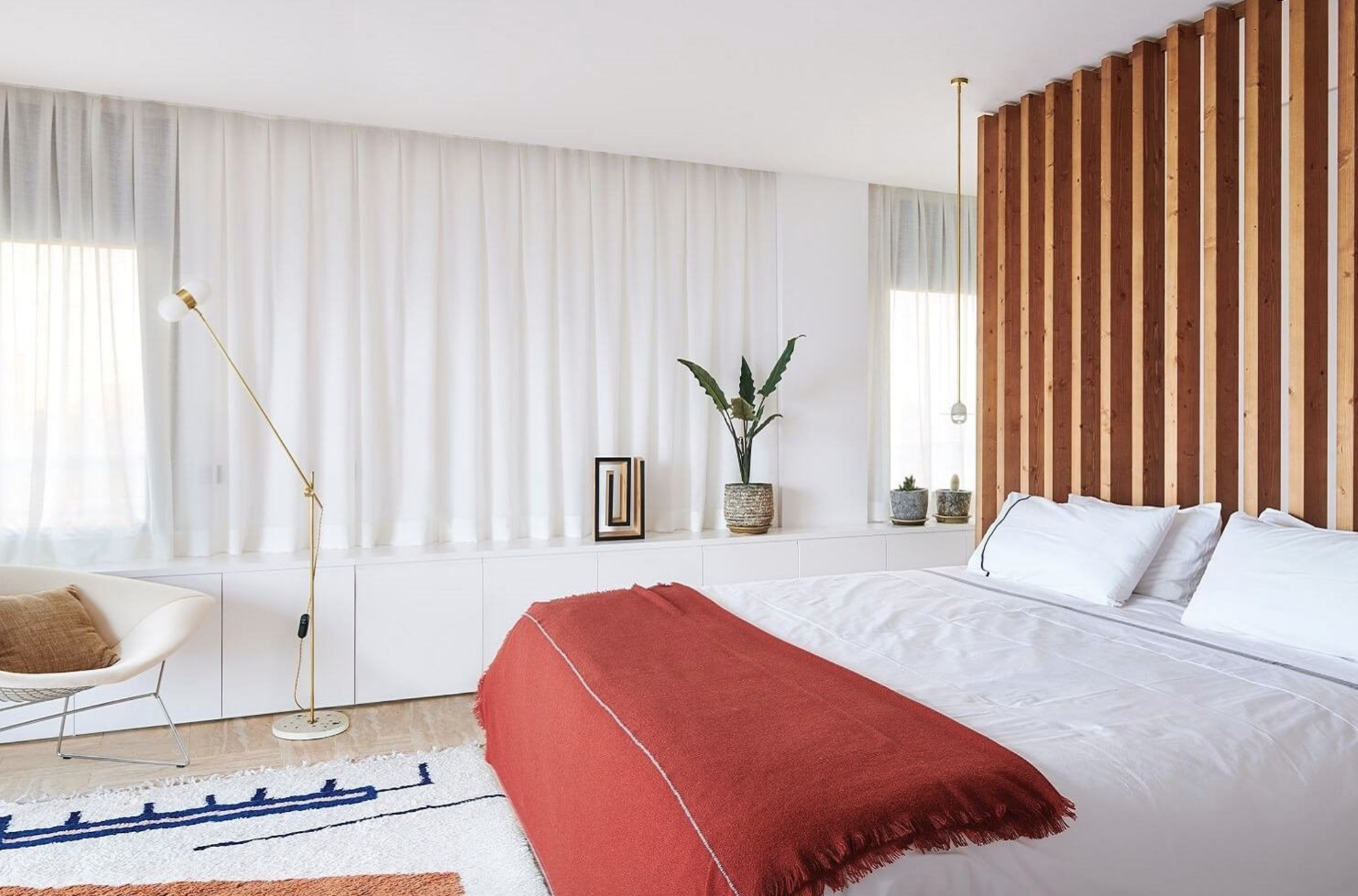 dormitorio blanco con colcha roja y cabecero separador de madera